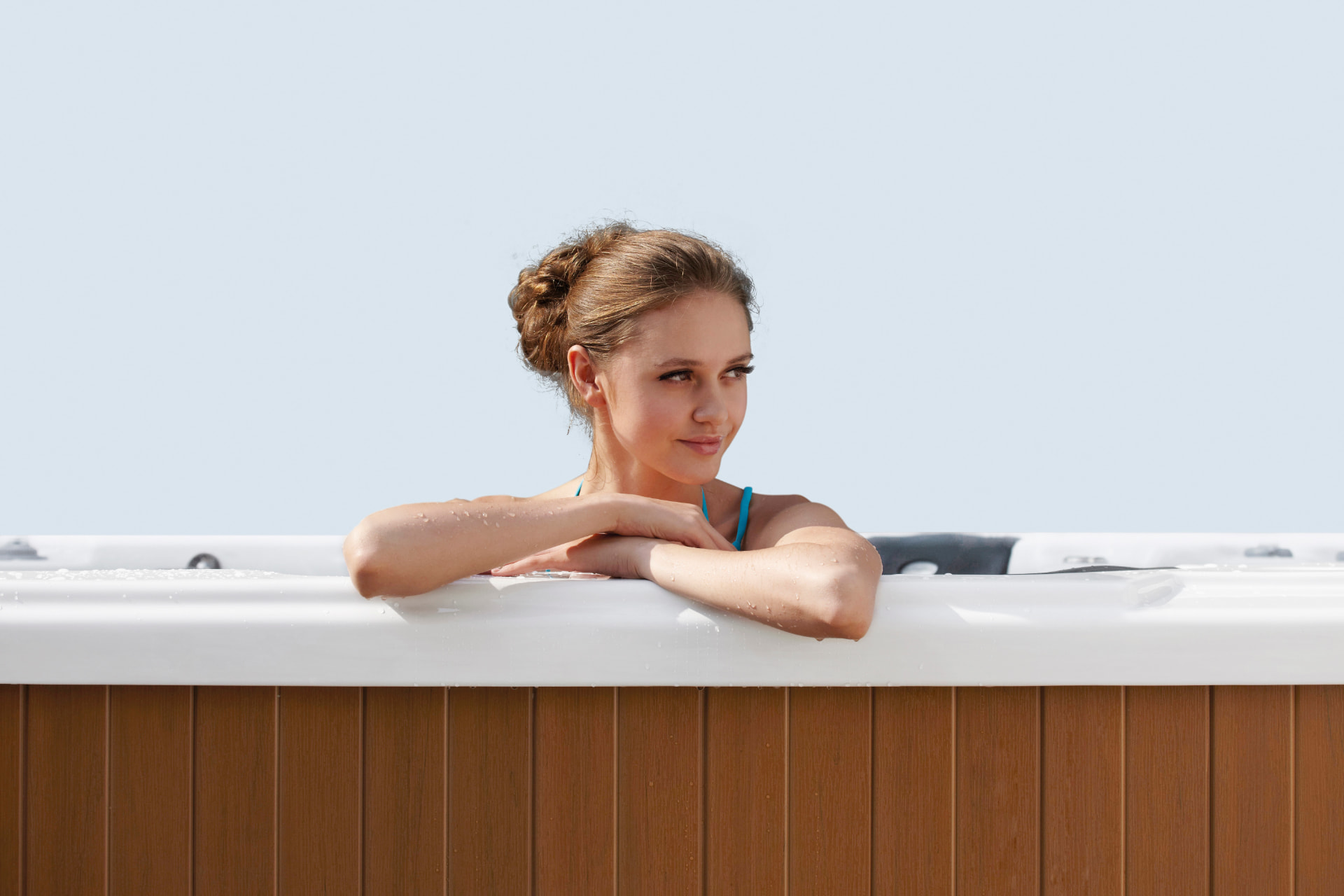 Woman resting her arms on the edge of a timber-clad spa, looking out to the side